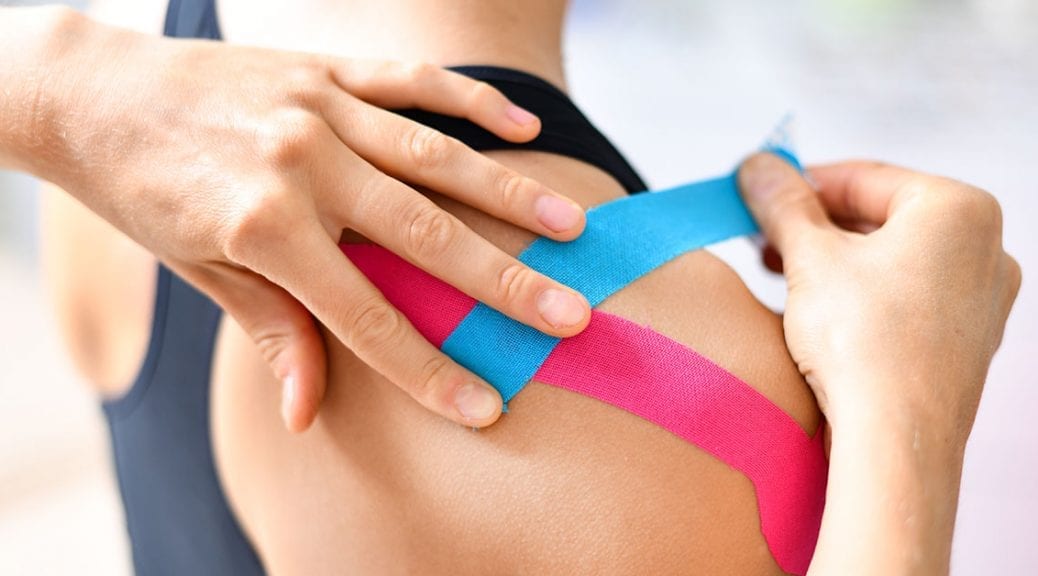 Kinesiology taping treatment with blue and pink tape on athlete patient injured arm. Woman hands apply kinesio treatment after sports muscle injury; blog: 5 Sports Injury Treatments