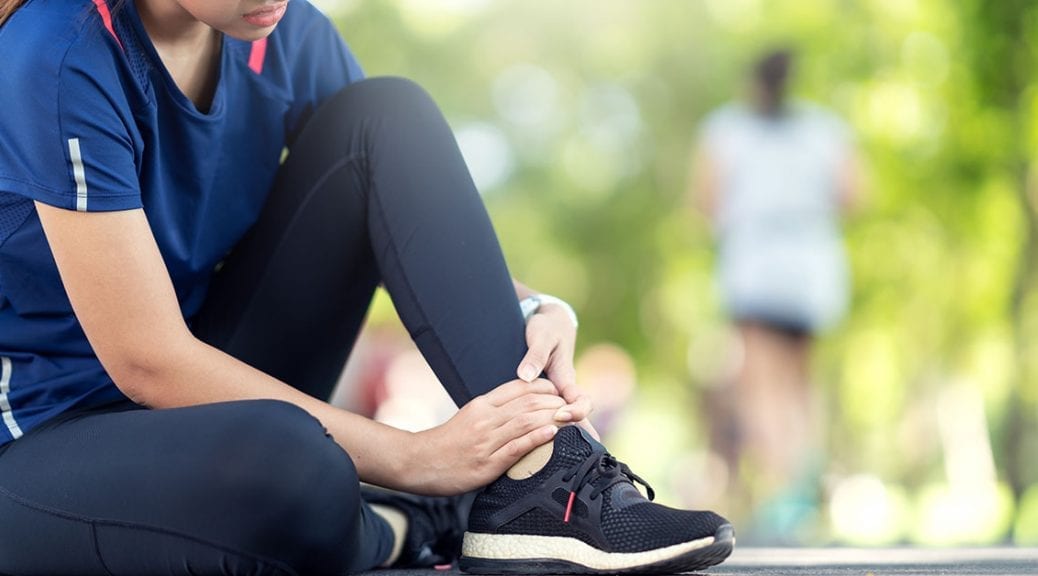 Young asian woman suffering ankle injury. Runner girl is injured by sprain ankle while running or exercising. Female runner touching foot in pain due to sprained ankle. Injury from workout concept; blog: difference between sprains and strains