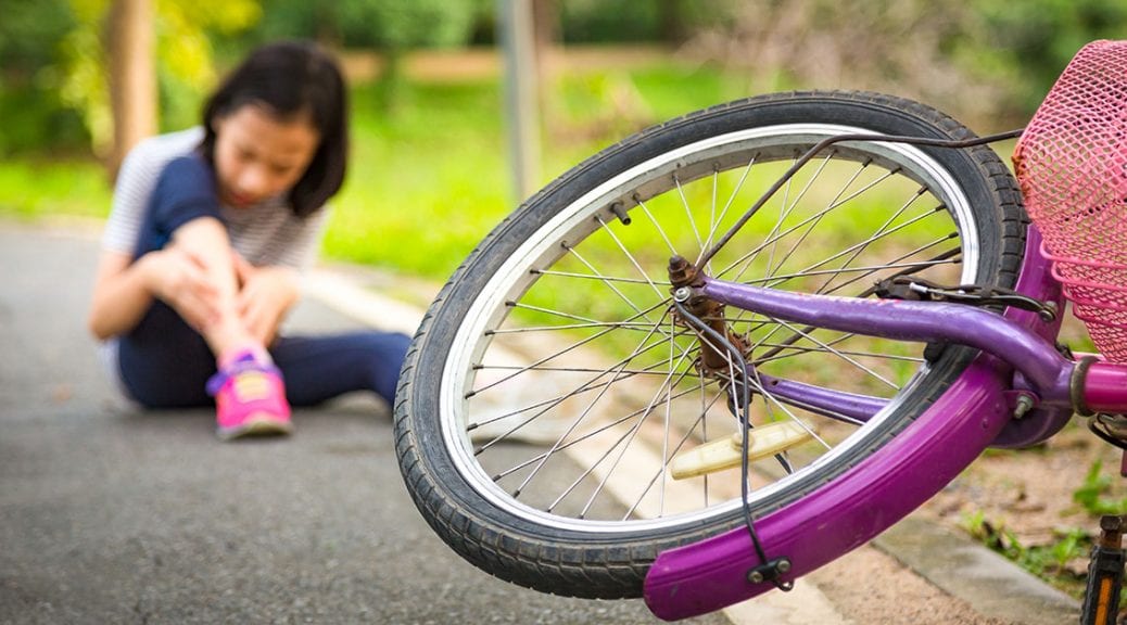 Asian little girl sitting down on the road with a slight sore leg pain due to a falling bicycle accident,the bike fall in front of the child at the park,falling bicycle,Accident concept; blog: 6 Tips for Avoiding Summer Sports Injuries
